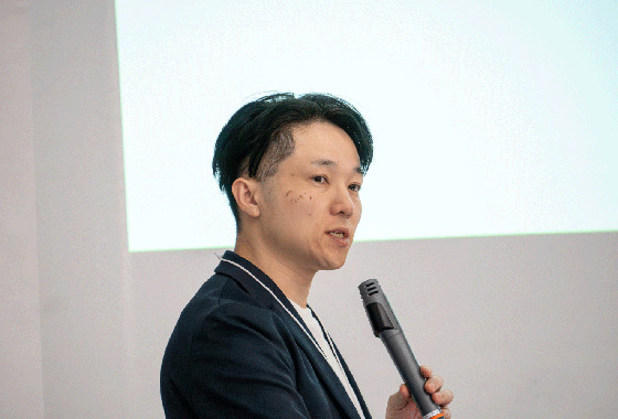 登壇者がマイクで日本地図のスライドを指し示し、2024年の地震発生地点を解説している様子。