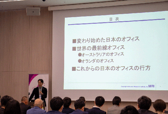 登壇者が、スライド画像を投影しながら、マイクを持ち解説している様子