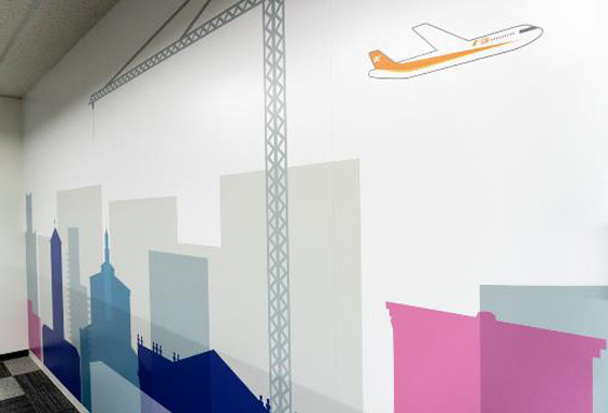 カラフルな建物のシルエットと飛行機が描かれたラクスのオフィスの壁のデザイン。